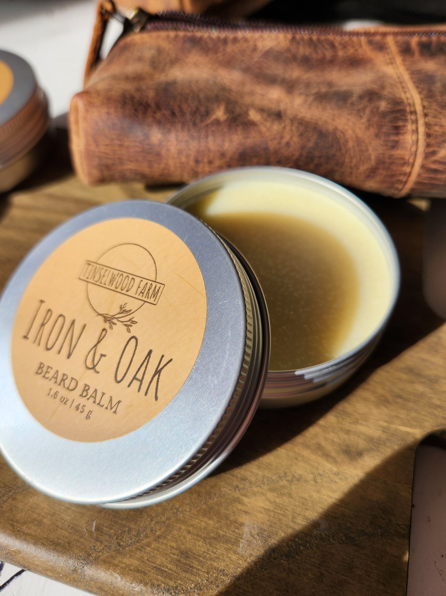 tin of Iron & Oak beard balm on a wooden surface with a leather pouch in background.