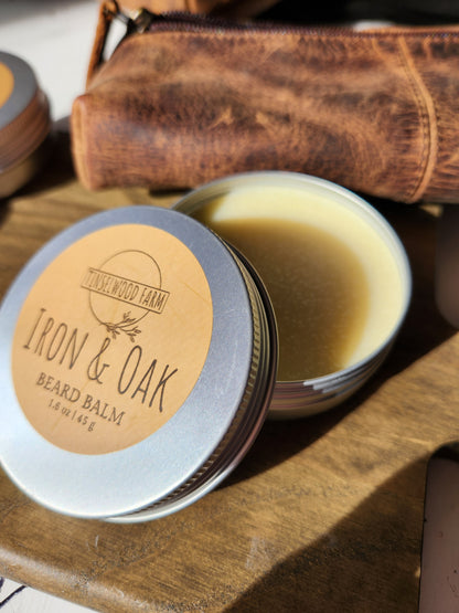 tin of Iron & Oak beard balm on a wooden surface with a leather pouch in background.