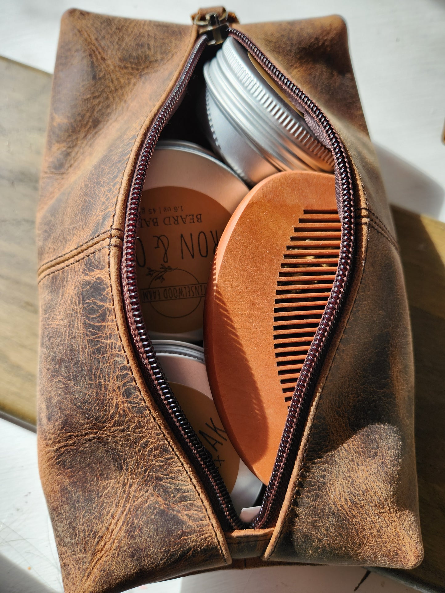 Brown leather toiletry bag with grooming products and a comb on a light background