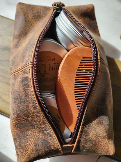 Brown leather toiletry bag with grooming products and a comb on a light background