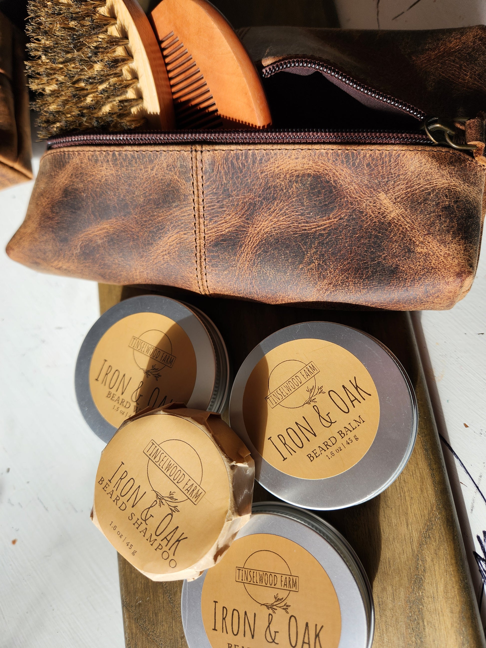 Set of grooming products including a leather bag, brushes, and tins labeled 'Iron & Oak' on a wooden tray.